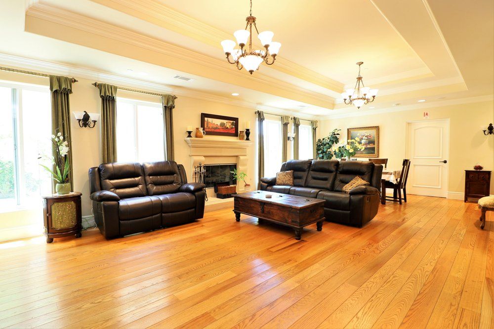 A spacious living room with elegant furnishings, featuring leather sofas, a central coffee table, a fireplace, and stylish chandeliers.