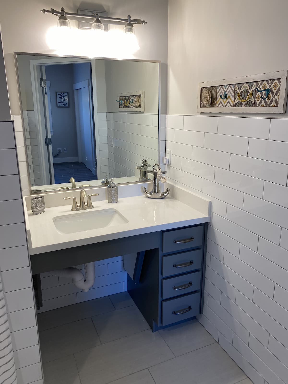 A small bathroom vanity with a mirror and sink, featuring white tiles and a decorative wall piece.