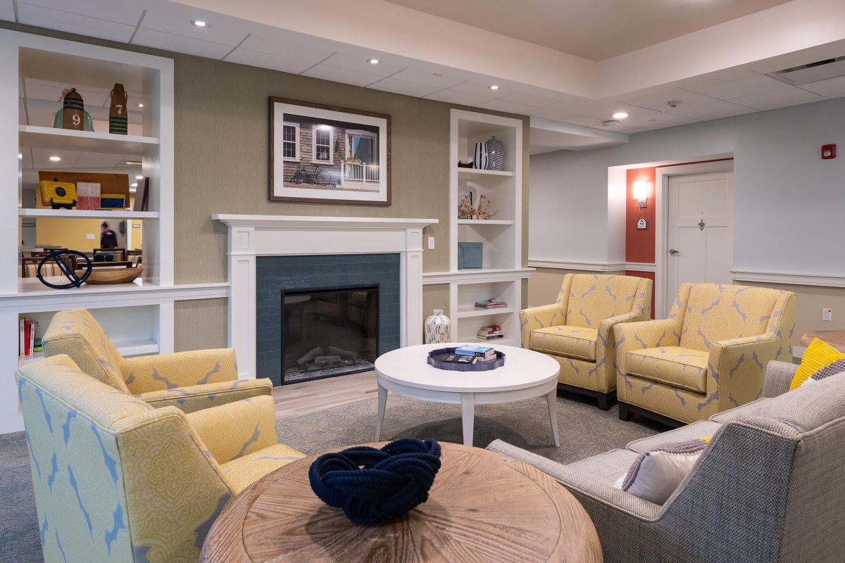 A cozy living room with a fireplace, featuring yellow armchairs and coffee tables surrounded by built-in shelves.