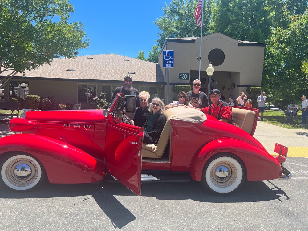 A group of people posing next to a vintage red convertible on a sunny day.