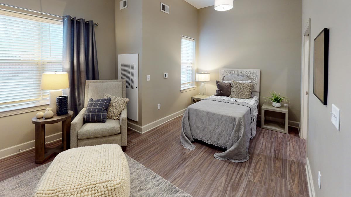 A modern and cozy bedroom with a single bed, armchair, and soft lighting.
