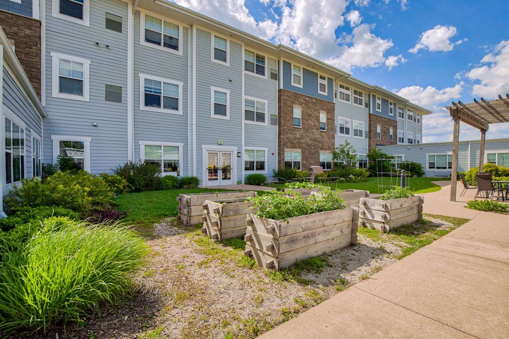 A modern residential apartment building with a landscaped garden and wooden planters under a sunny sky.
