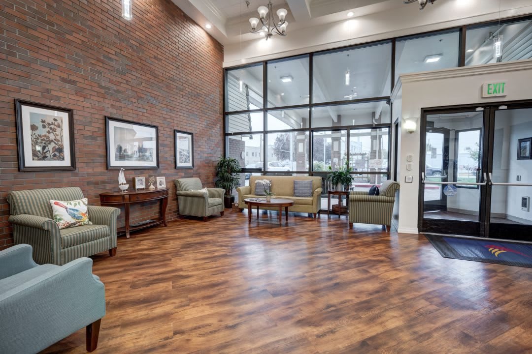 A modern lobby with comfortable seating and large windows, featuring a wooden floor and brick accent wall.