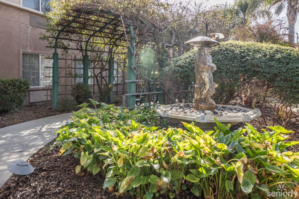 A serene garden scene featuring a fountain with a statue surrounded by lush foliage and an arched trellis.