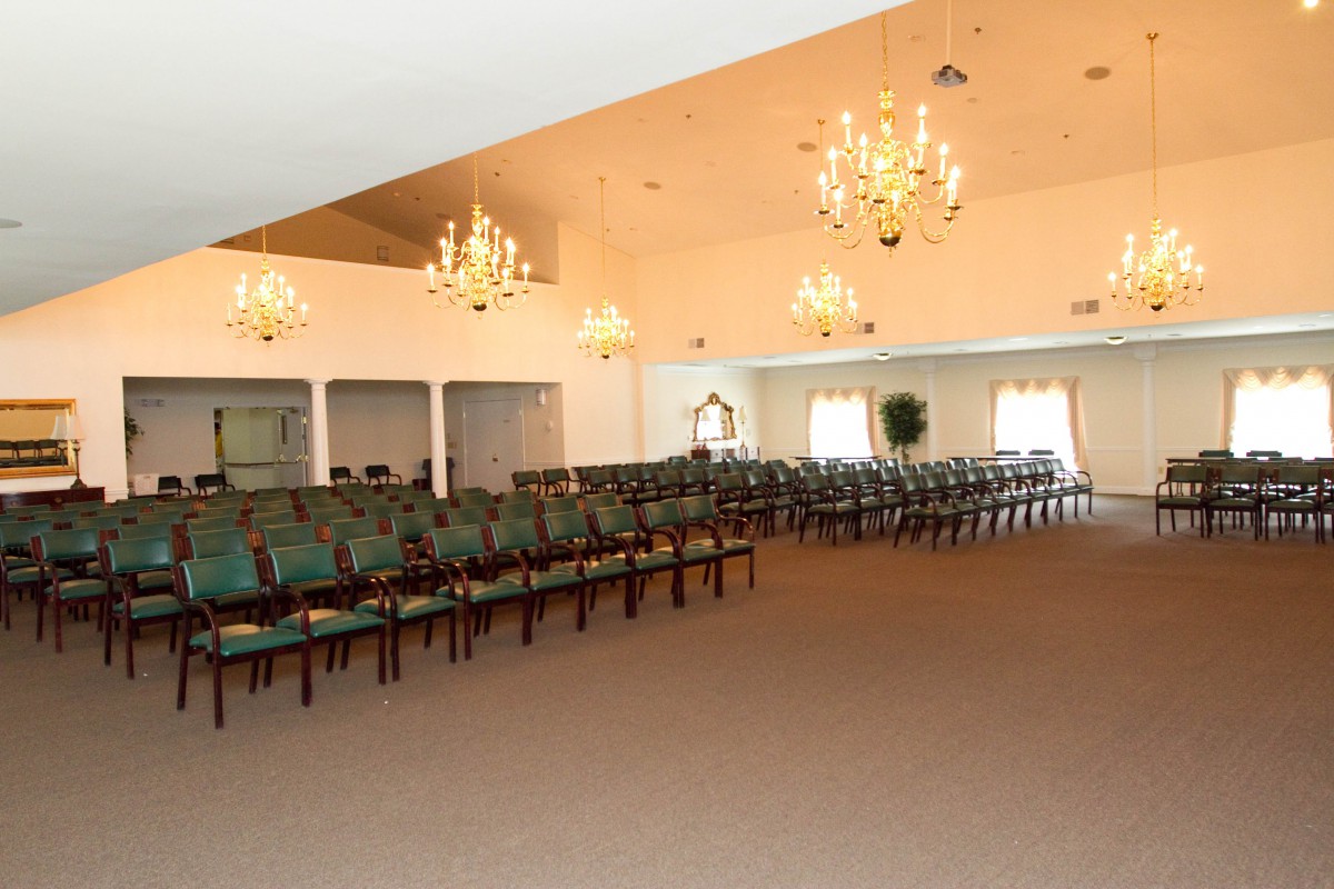 Spacious event hall with rows of chairs and elegant chandeliers.