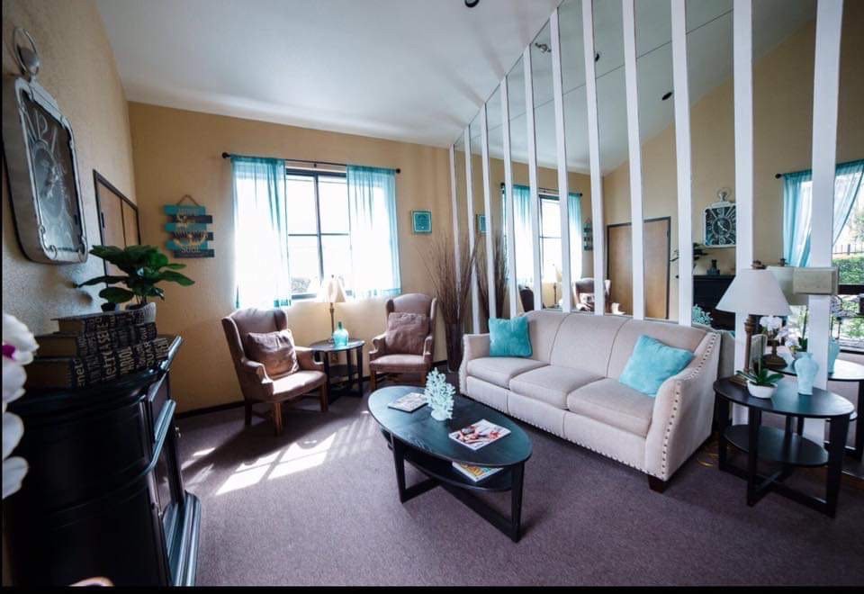 A cozy living room with a sofa, two chairs, and a coffee table, accented by natural light from a window with blue curtains.