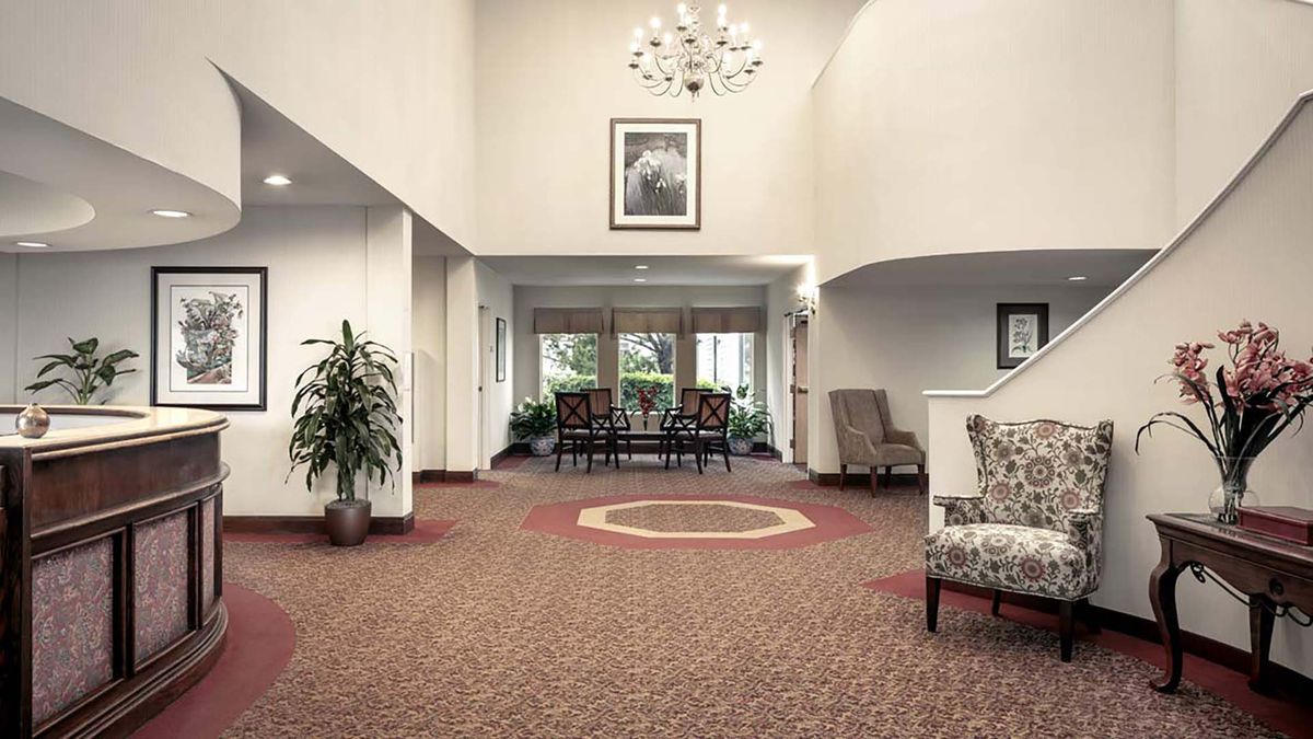 A spacious lobby with elegant decor, featuring a chandelier, carpeted floors, and a comfortable seating area.