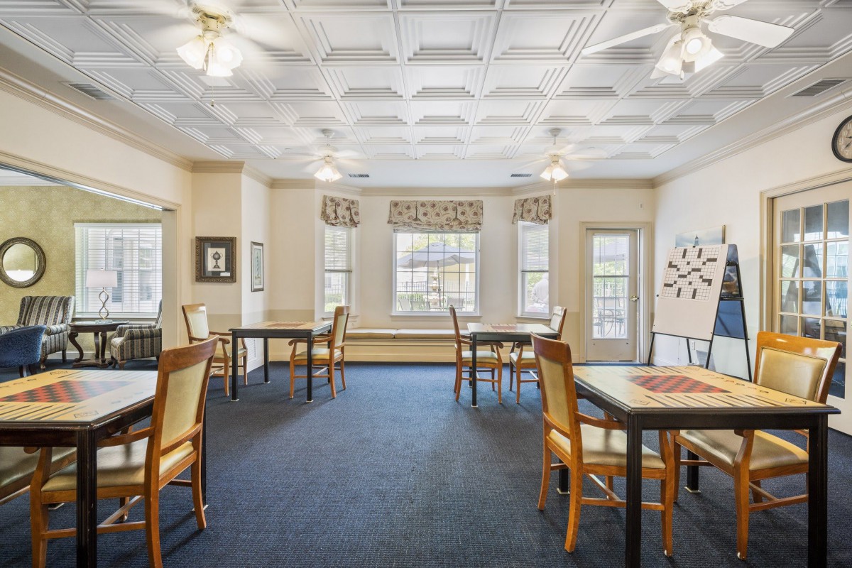 A bright dining room with multiple tables and chairs, featuring ceiling fans and large windows.