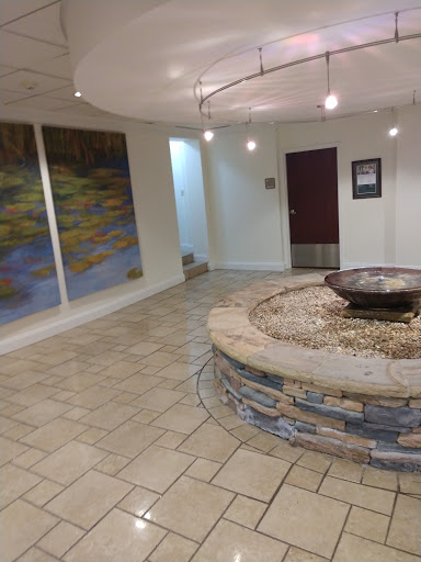 A serene interior lobby featuring a circular water fountain and artistic wall murals.
