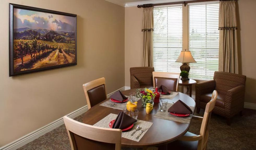 A cozy dining room with a round table set for a meal, featuring neatly arranged place settings and a decorative lamp by the window.