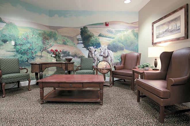 A cozy living room with a mural of a pastoral scene, featuring comfortable furniture and decorative elements.