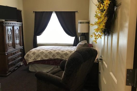 A cozy bedroom with a bed, armchair, and window with curtains.
