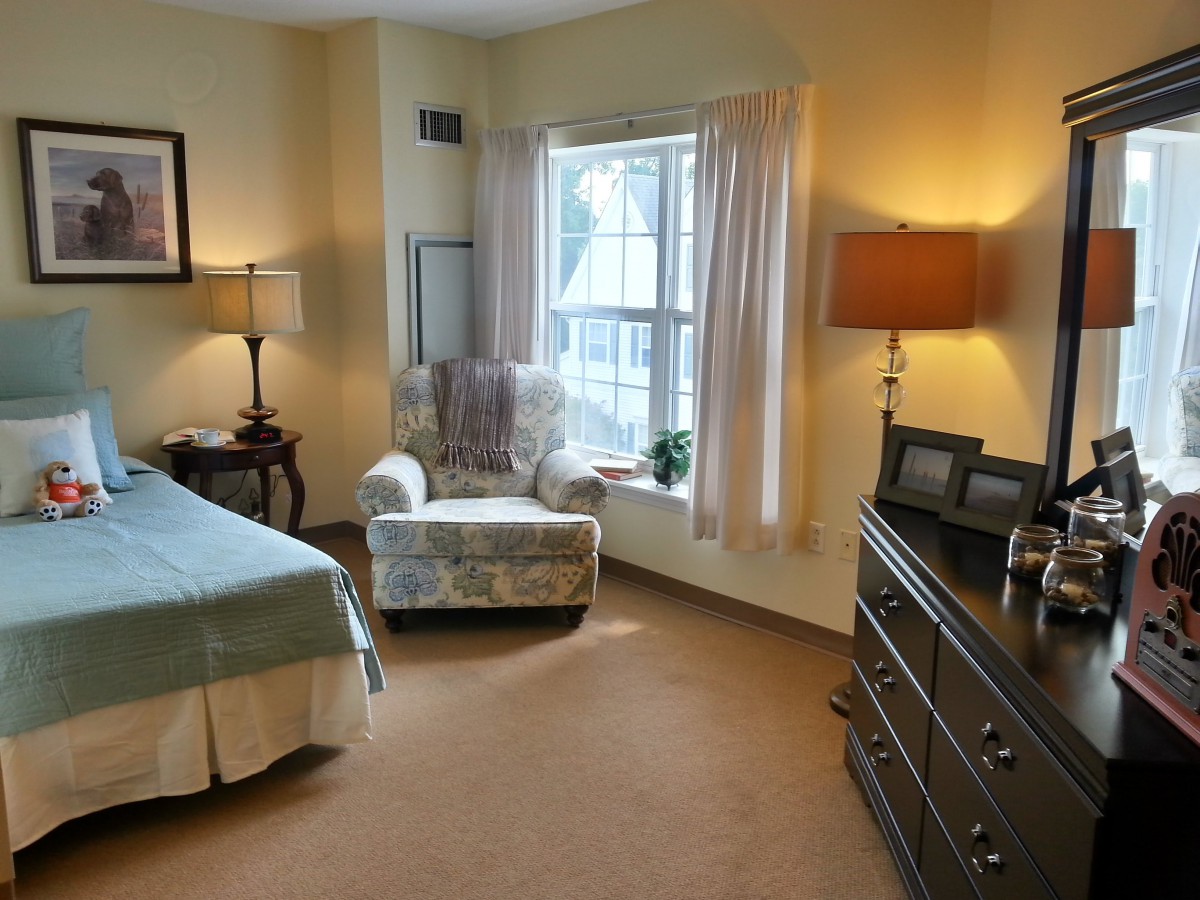 A cozy bedroom with an armchair by the window, a bed, and warm lighting.