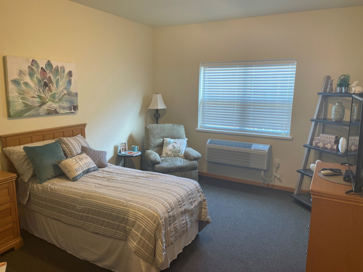 A cozy bedroom with a single bed, armchair, and soft lighting.