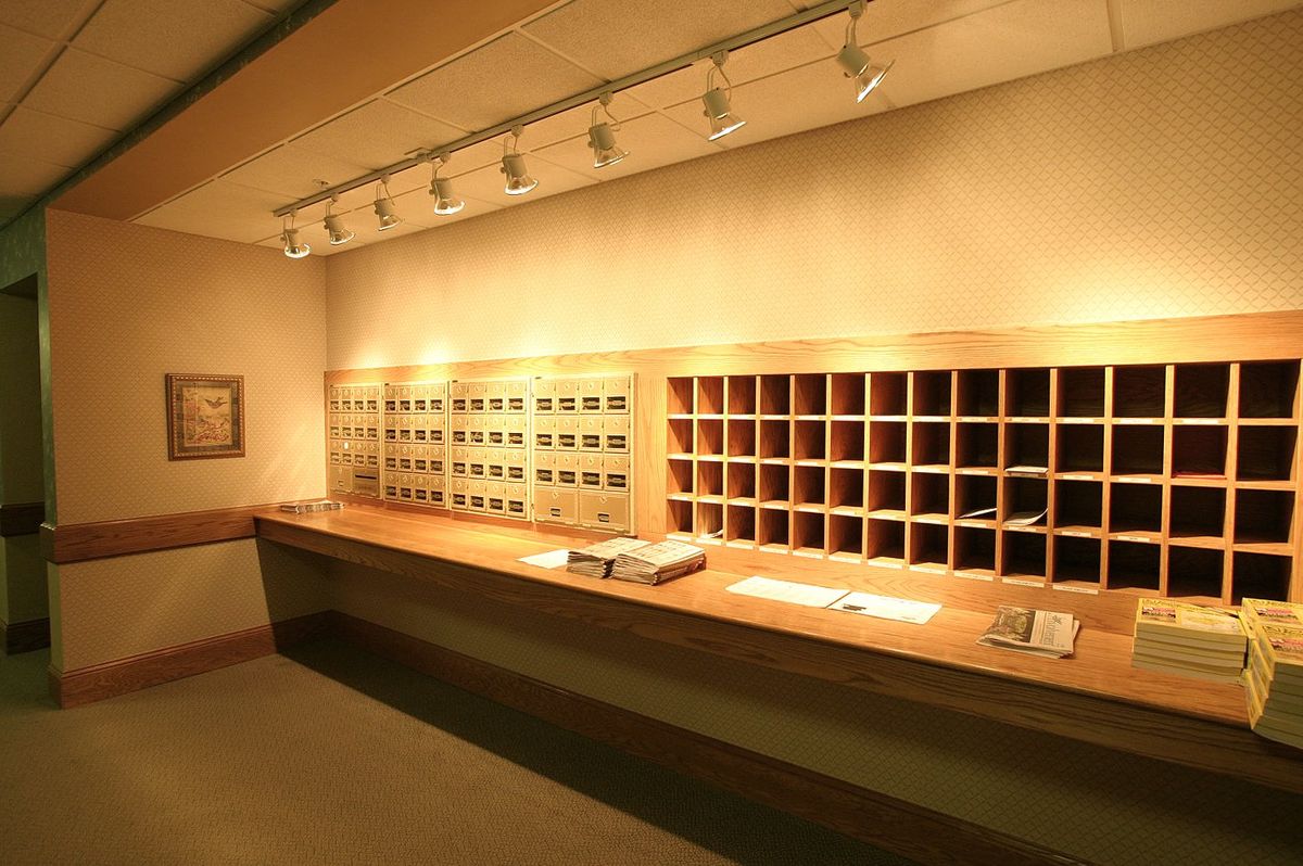 A hotel reception desk featuring a wooden counter with mail slots and overhead lighting.
