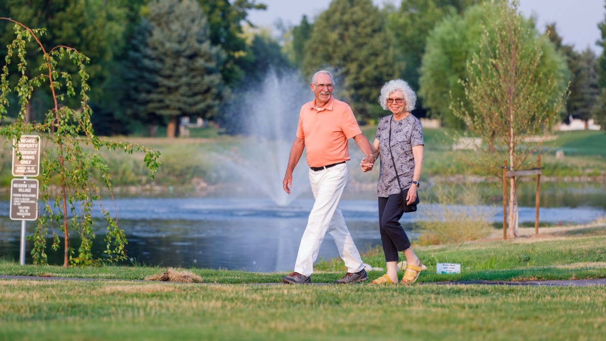 An elderly couple enjoying a walk in the park near a pond and fountain.