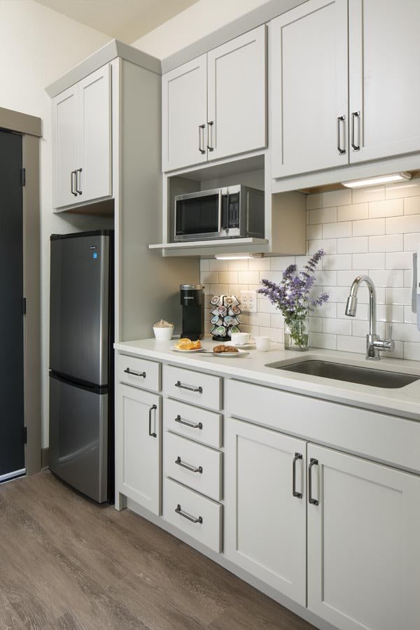 A modern kitchen interior featuring sleek cabinetry, a microwave, refrigerator, coffee maker, and a clean countertop with a decorative plant.