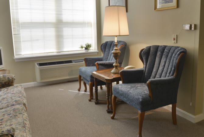 A cozy living room corner with two blue chairs and a lamp by the window.