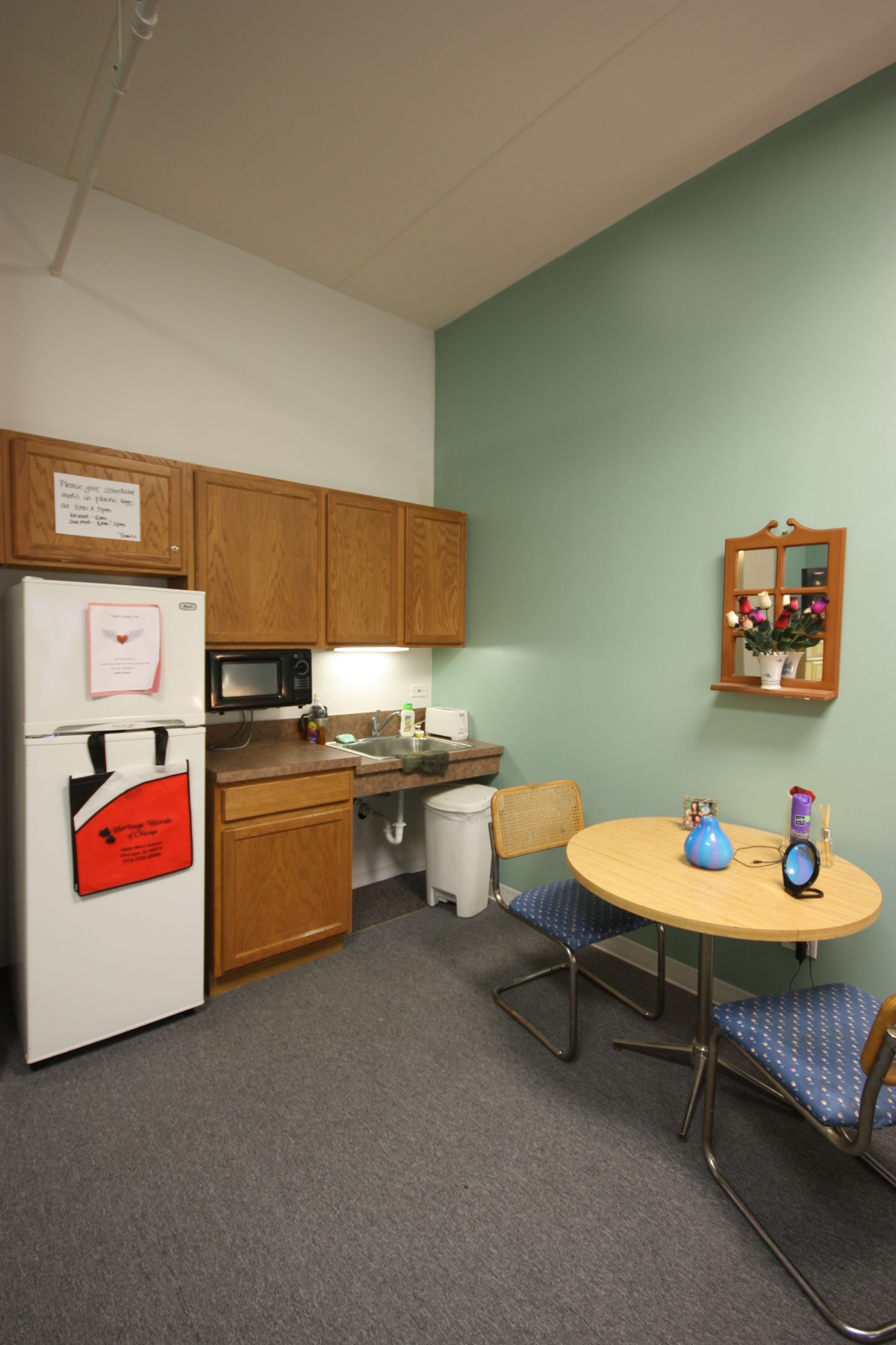 A small break room with a kitchenette, featuring a refrigerator, microwave, and a round table with chairs.
