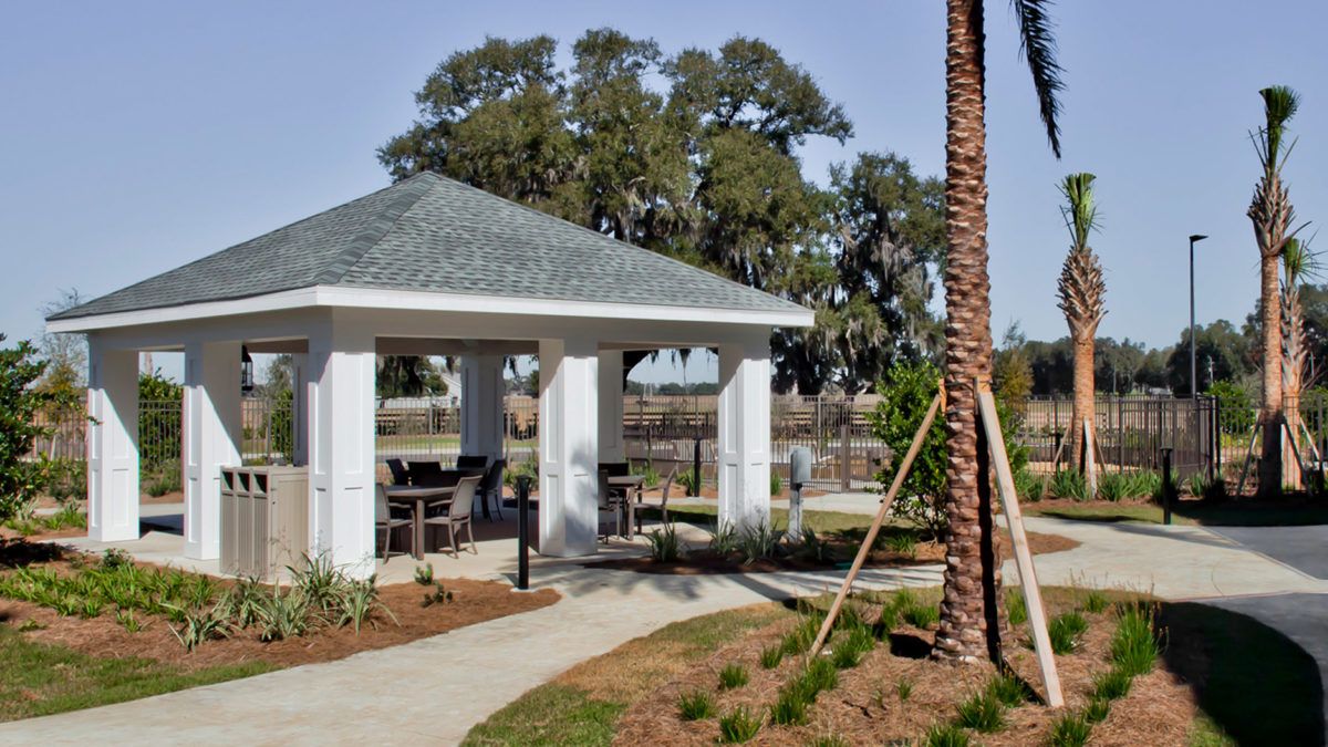 A gazebo with outdoor seating set in a landscaped park area featuring palm trees and pathways.