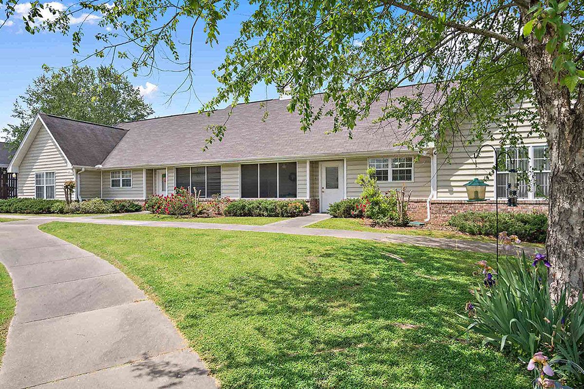 A single-story house with a well-maintained lawn and driveway, surrounded by trees.
