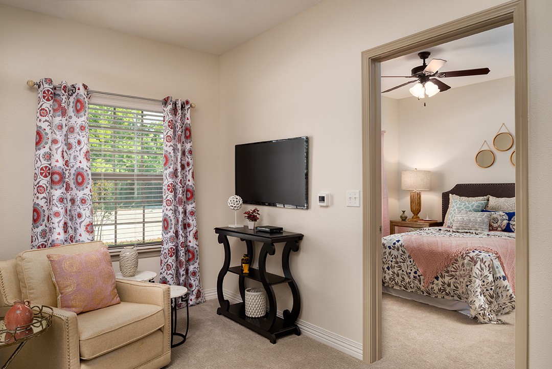 A cozy living room with a television and sofa, leading into a tastefully decorated bedroom.