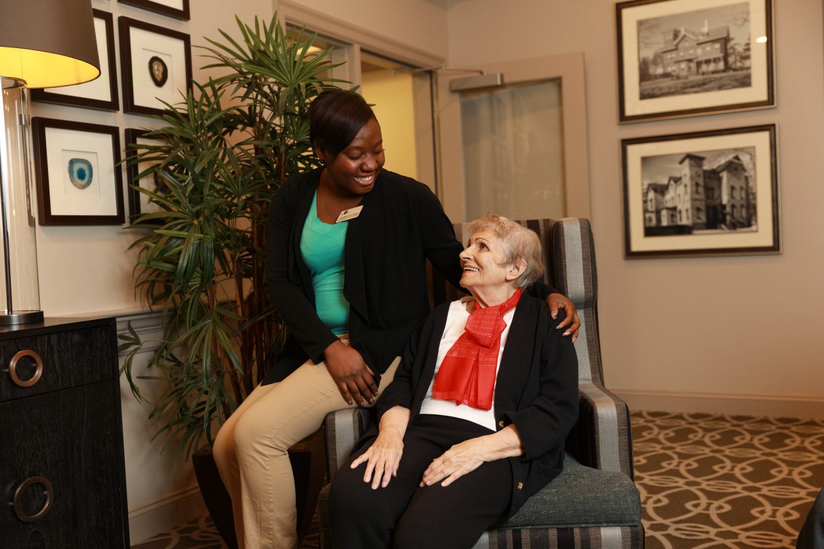 A caregiver interacts warmly with an elderly woman in a nursing home setting.