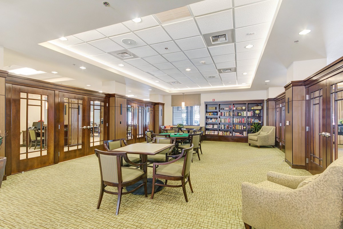 A well-lit room with tables and chairs, featuring a wall of bookshelves.