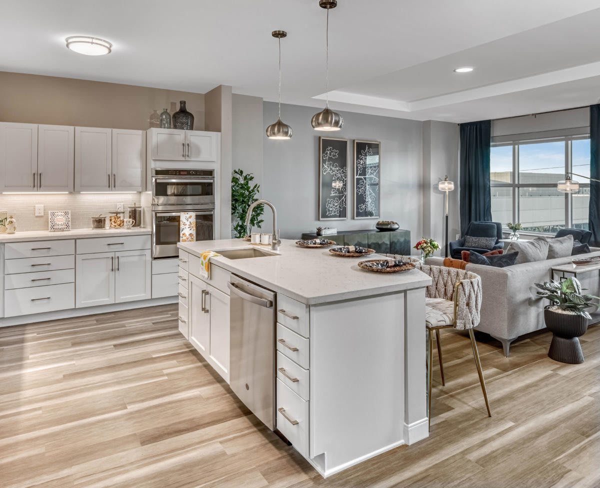 A modern open-concept kitchen and living area featuring a central island with white cabinetry and wood flooring.