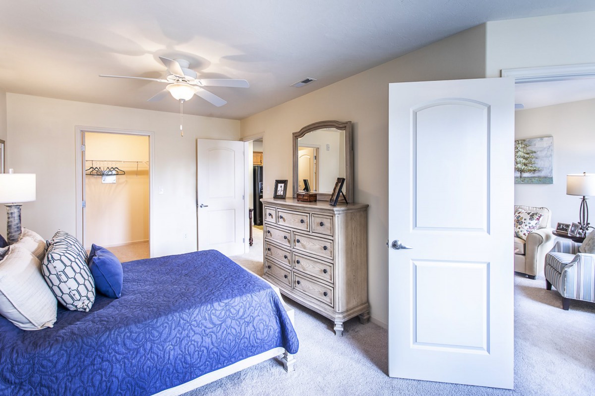 A cozy bedroom with a blue bedspread and wooden dresser featuring a mirror.