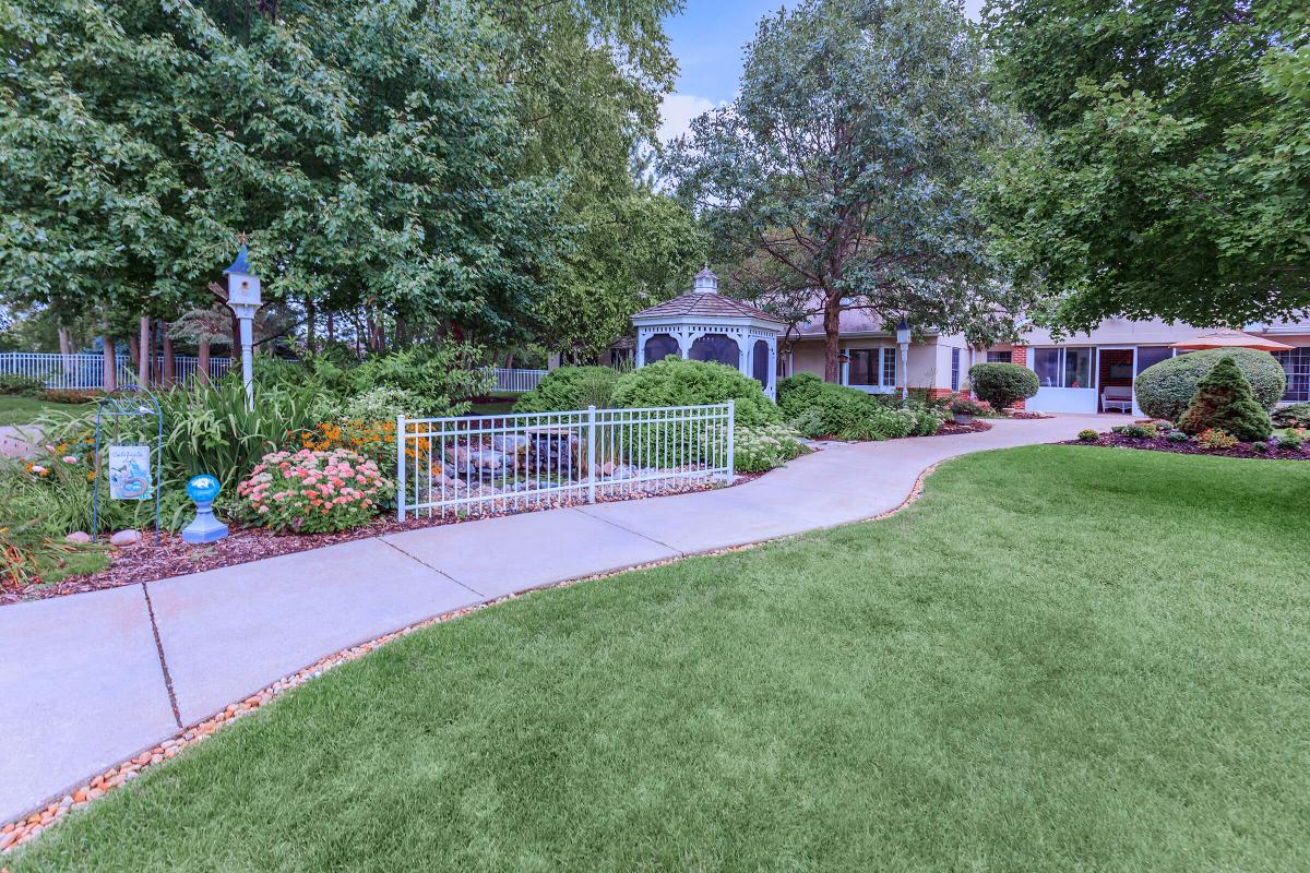 A beautifully landscaped garden with a winding pathway leading to a quaint building surrounded by trees and flowers.