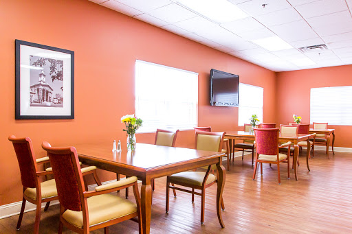 A cozy dining area with orange walls and comfortable seating, featuring natural light and a television.