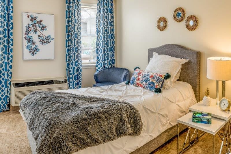 A cozy bedroom with stylish decor, featuring a neatly made bed, decorative pillows, and patterned curtains.