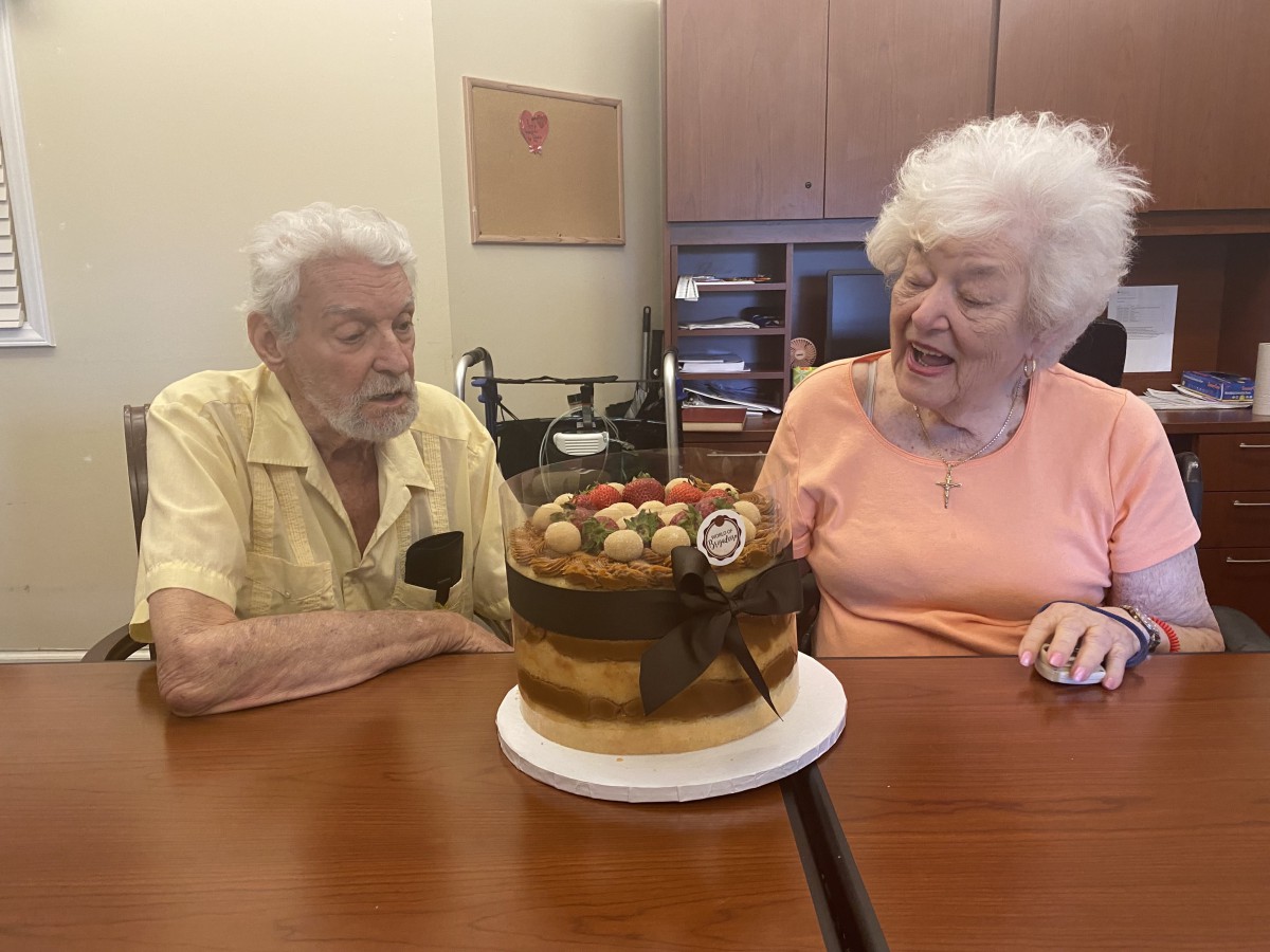 An elderly couple sitting at a table with a beautifully decorated birthday cake.