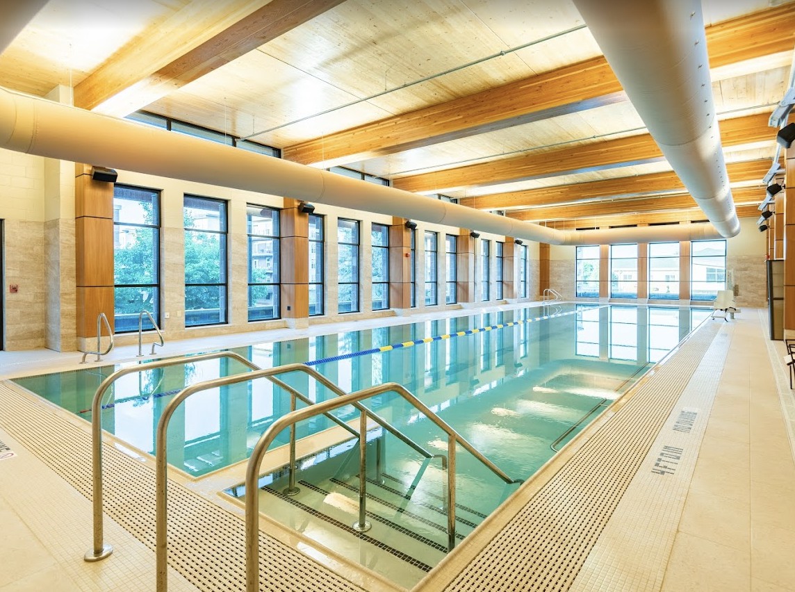 A modern indoor swimming pool with ample natural light and wooden accents.