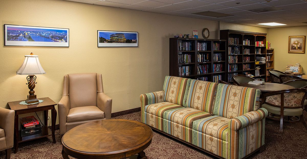 A cozy living room with a striped sofa, an armchair, a wooden coffee table, and a bookshelf filled with books.