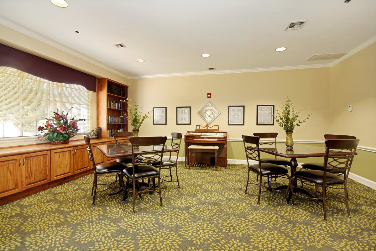 A cozy dining area with tables, chairs, and a piano against a decorated wall.
