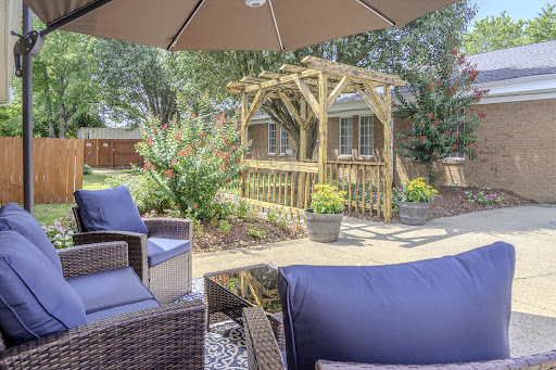 A cozy outdoor patio setup featuring comfortable seating and a wooden archway in a lush garden.