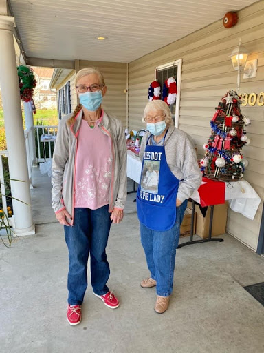 Two women wearing masks stand together outside, surrounded by festive decorations.
