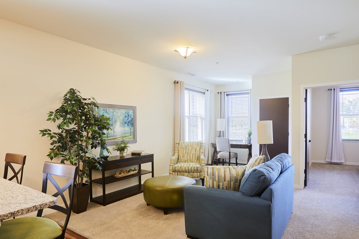 A cozy living room with a sofa, chairs, and a coffee table, decorated with plants and artwork.