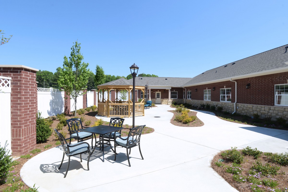 A sunny outdoor patio area with a gazebo and seating surrounded by landscaped pathways.