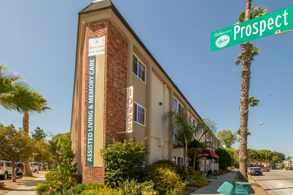 A residential building on a street corner with a visible street sign and landscaping in front.