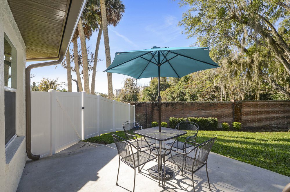 A backyard patio with a table, chairs, and a large umbrella under a clear blue sky.