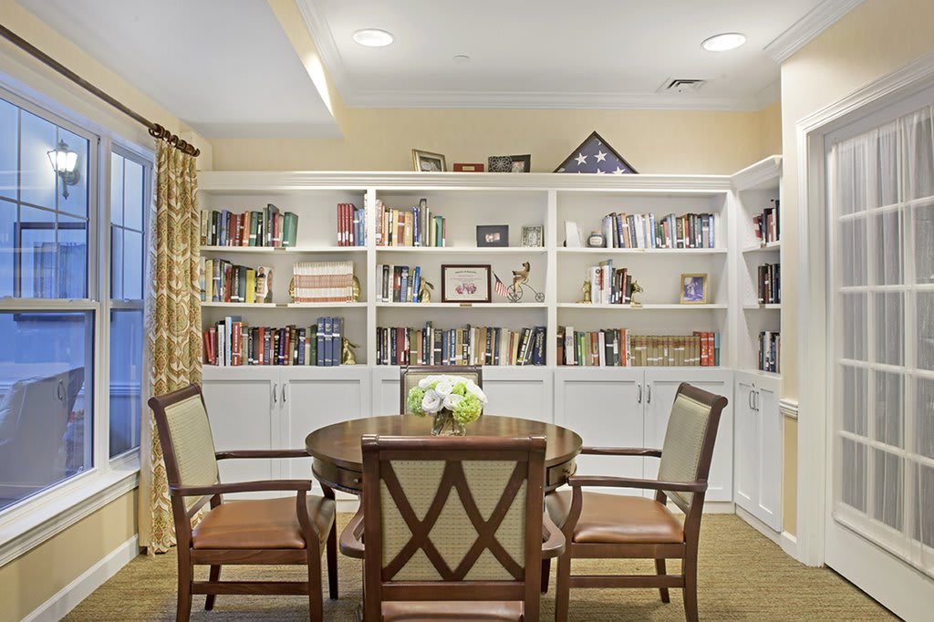 A cozy library room with a round table and chairs surrounded by bookshelves filled with books.