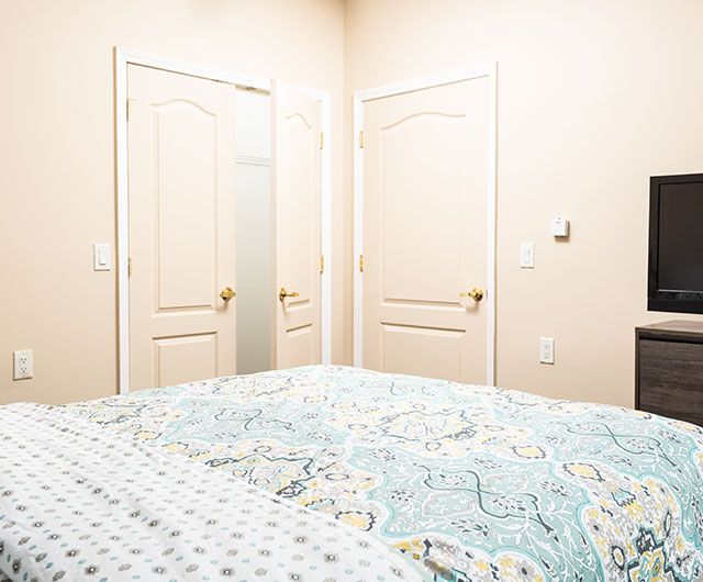 A neatly arranged bedroom featuring two closed doors and a bed with patterned bedding.