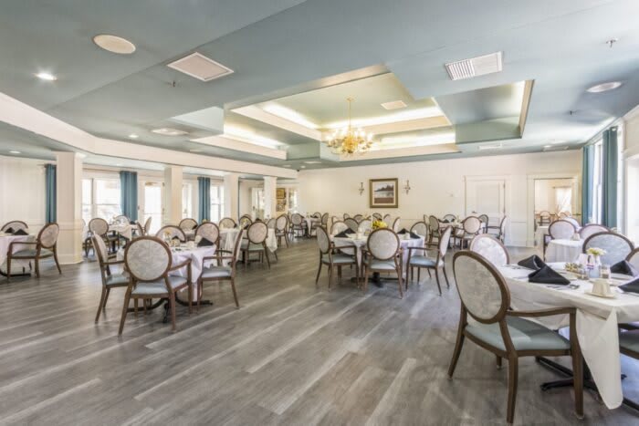 An elegant dining room with neatly arranged tables and chairs, featuring a light blue ceiling and large windows.