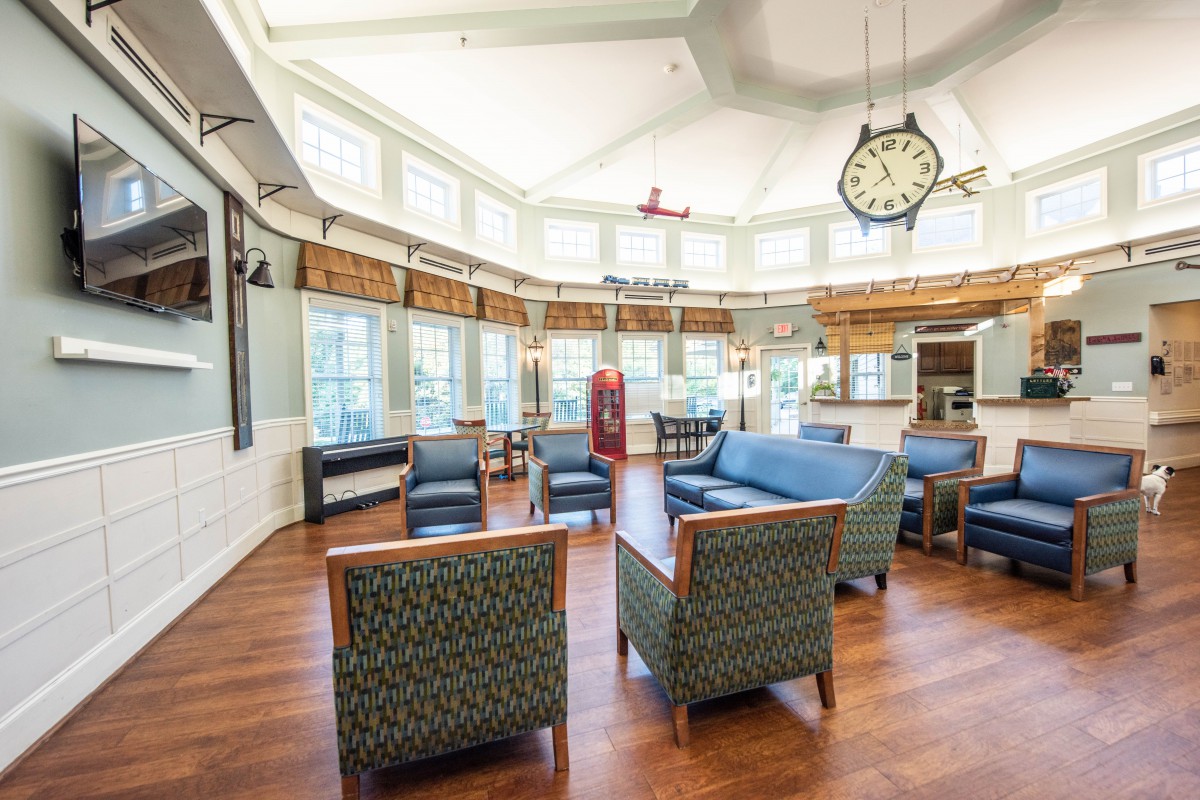 A spacious lounge with comfortable seating, large windows, and a prominent clock on the wall.