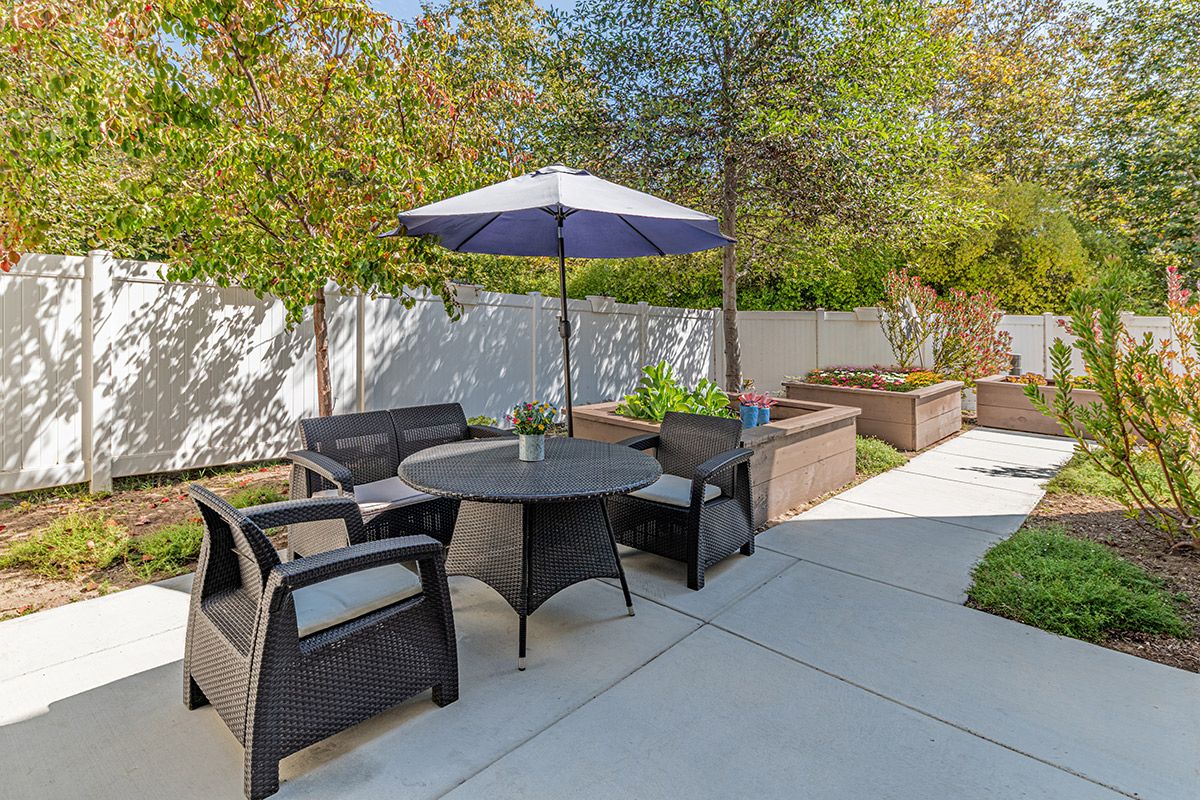 A cozy patio area with seating, a table, and an umbrella in a garden setting.