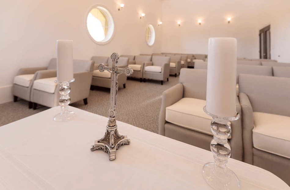 Interior of a chapel with a cross and candles on an altar, surrounded by seating.