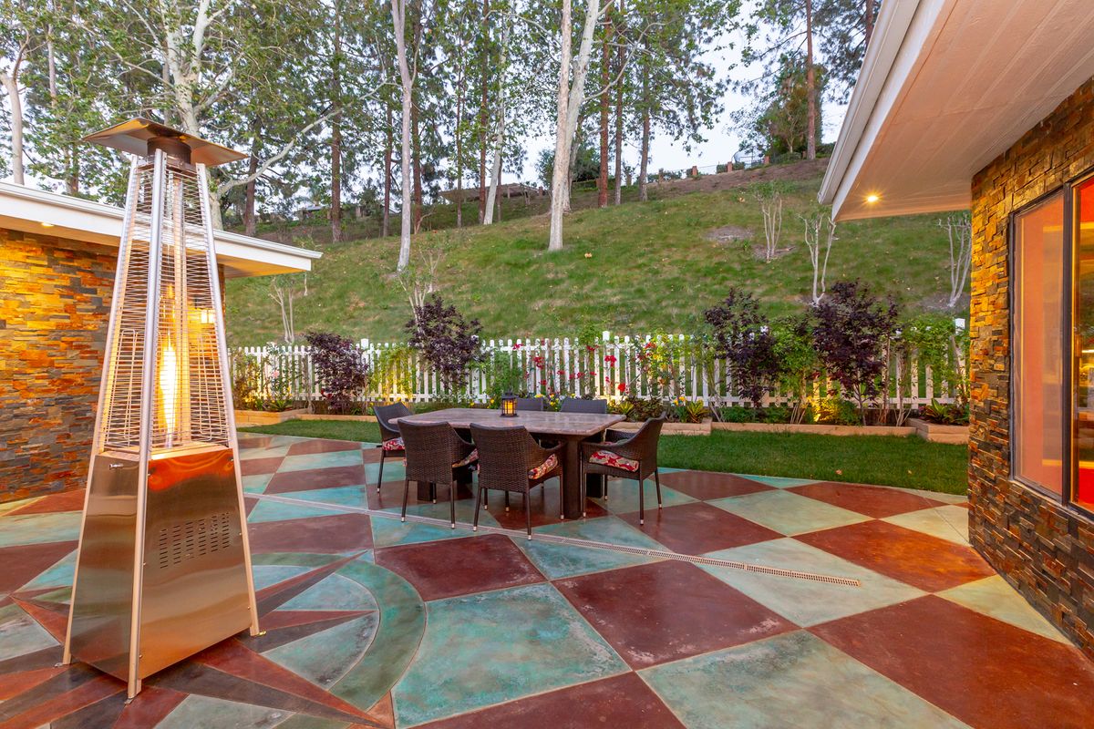 A cozy outdoor patio with a colorful checkered floor, surrounded by lush greenery and illuminated garden lights.
